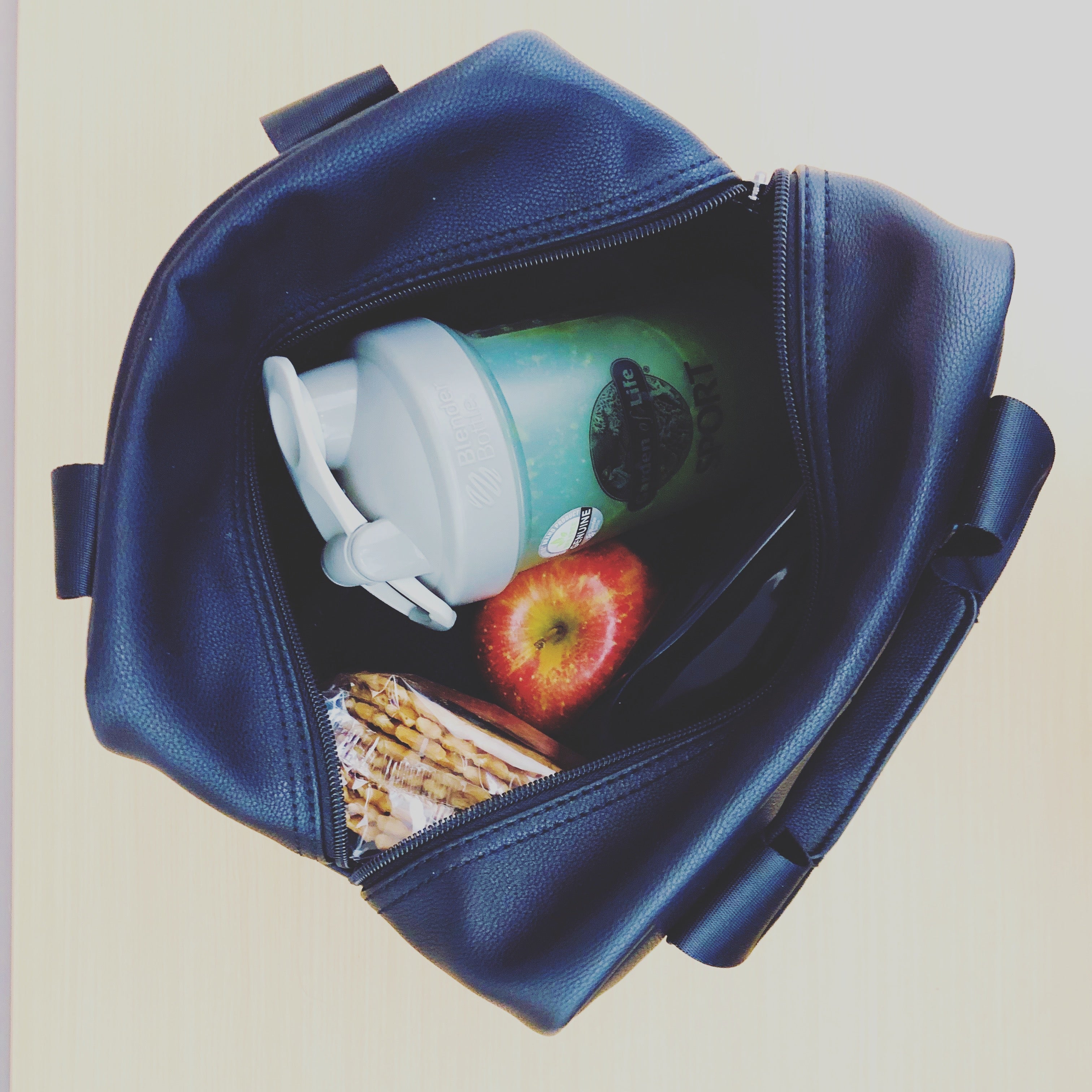 top view of an open T|W lunch tote with crackers, an apple and resusable water bottle