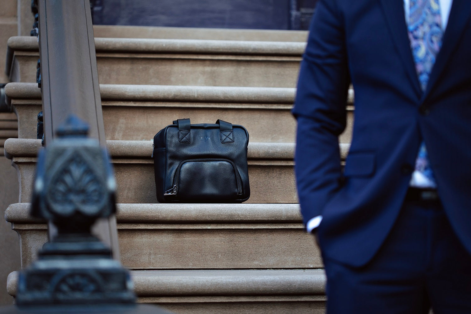 T|W lunch tote, in black, sitting on a step with a man in a suit, in front of the image